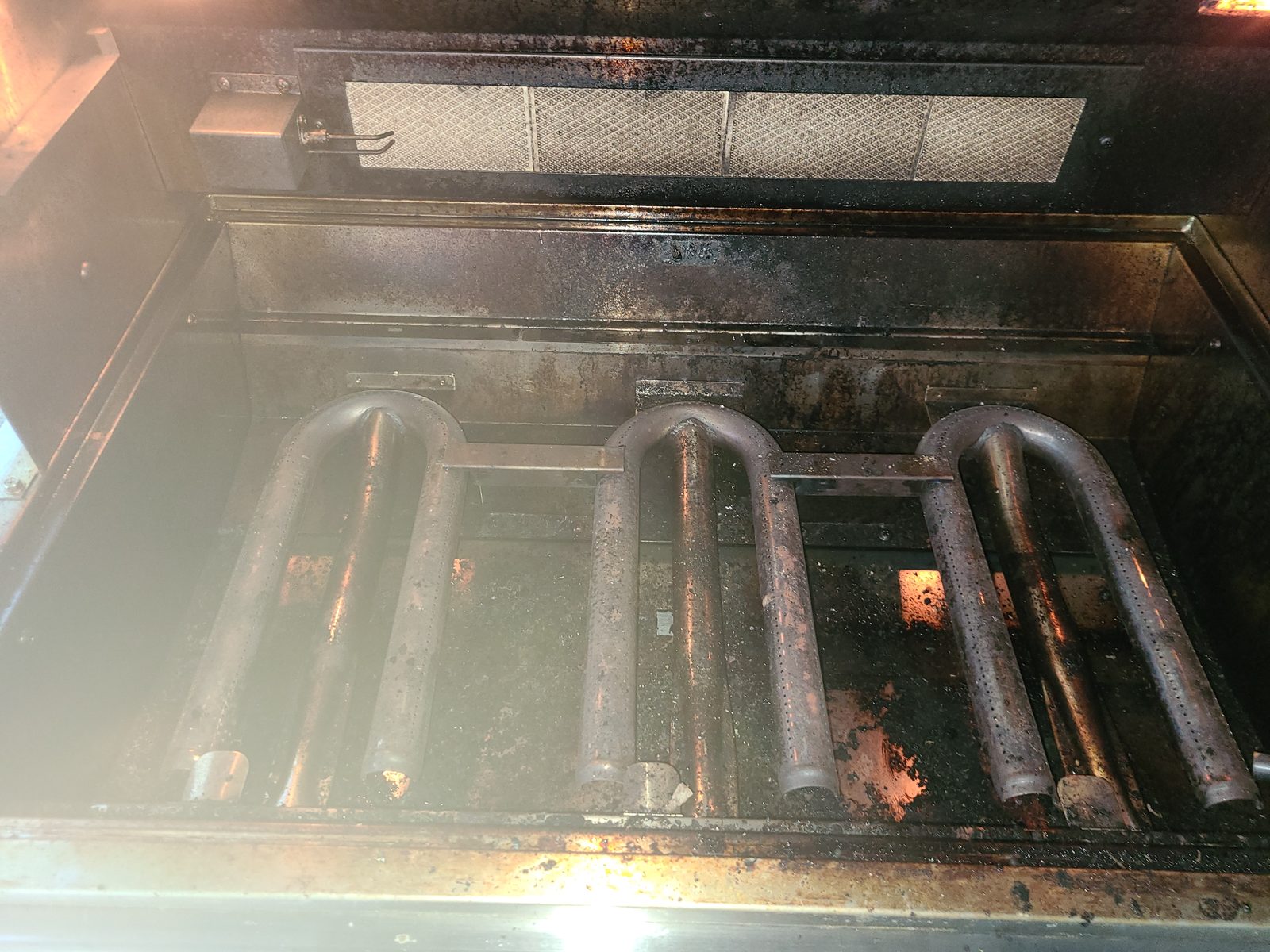 Dirty luxury built-in grill burner chamber with heavy carbon buildup and grease — before professional grill cleaning in Bradenton FL